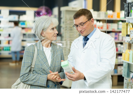 Man apothecary hold package with cream and talks with senior woman client about nuances of care Man apothecary hold package with cream and talks with senior woman client about nuances of care 142177477