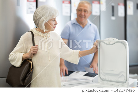 Elderly couple choosing top-loading washing machine at household appliances store Elderly couple choosing top-loading washing machine at household appliances store 142177480
