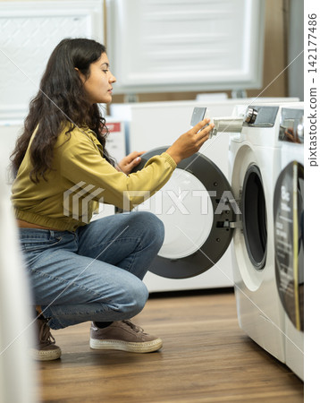 Young woman choosing washing machine at household appliances store Young woman choosing washing machine at household appliances store 142177486