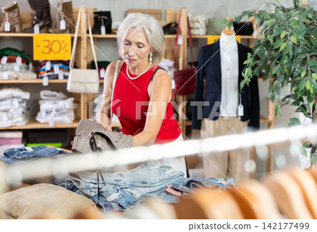Elderly woman choosing trousers in clothing store Elderly woman choosing trousers in clothing store 142177499