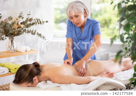 Elderly woman doing back massage to young woman Elderly woman doing back massage to young woman 142177584