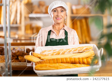 Smiling mature female seller showing assortment of bakery Smiling mature female seller showing assortment of bakery 142177615