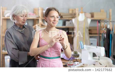 Mature tailoress measuring female client in sewing workshop Mature tailoress measuring female client in sewing workshop 142177682