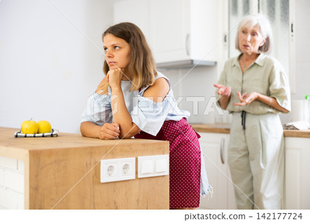 Upset girl at home kitchen while worried elderly mother reprimanding her. Family conflicts concept Upset girl at home kitchen while worried elderly mother reprimanding her. Family conflicts concept 142177724