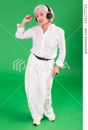 Elderly woman listening to music and dancing in front of green screen Elderly woman listening to music and dancing in front of green screen 142177725