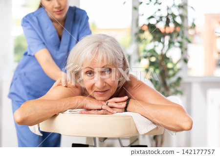 Cropped circumcised woman performs shoulder massage to female client. Cropped circumcised woman performs shoulder massage to female client. 142177757