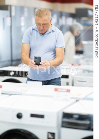Elderly man choosing washing machine scans QR code on the price tag to check the technical specifications Elderly man choosing washing machine scans QR code on the price tag to check the technical specifications 142177782