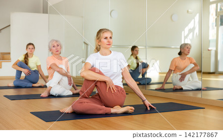 Portrait of woman practicing yoga in group, making twisting asana Portrait of woman practicing yoga in group, making twisting asana 142177867