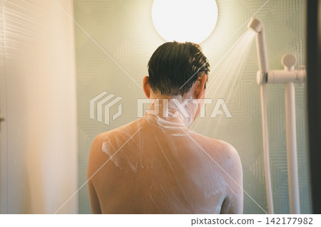 A man's shower time, washing his back while taking a shower. A man's shower time, washing his back while taking a shower. 142177982