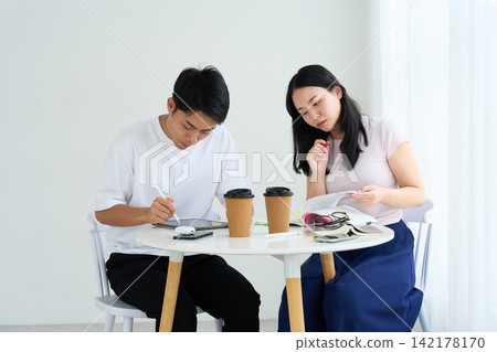 正在使用平板電腦和教科書學習的男女。 正在使用平板電腦和教科書學習的男女。 142178170