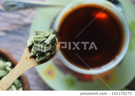 Cardamom beside a cup of tea on a wooden table Cardamom beside a cup of tea on a wooden table 142178275