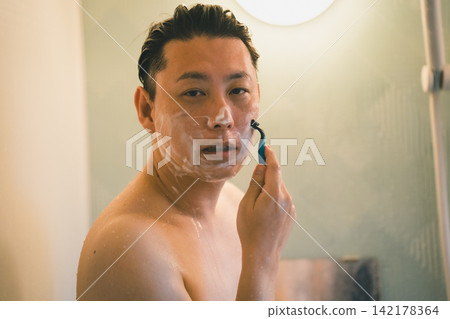 一名40歲男子在洗澡時於淋浴間刮鬍子。 一名40歲男子在洗澡時於淋浴間刮鬍子。 142178364