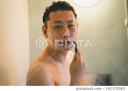 一名40歲男子在浴室淋浴時刮鬍子。 一名40歲男子在浴室淋浴時刮鬍子。 142178365