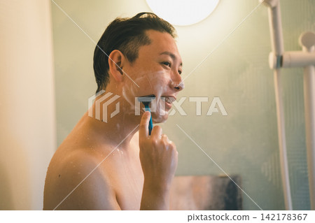 一名男子在洗澡時面帶微笑地刮鬍子。 一名男子在洗澡時面帶微笑地刮鬍子。 142178367
