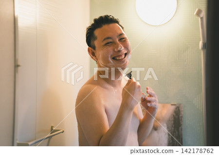 一位40歲的男子在洗澡時面帶笑容地刮鬍子。 一位40歲的男子在洗澡時面帶笑容地刮鬍子。 142178762