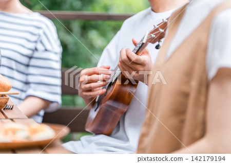 在一次燒烤露營之旅中,一名男子的手正在彈奏尤克里裡。 在一次燒烤露營之旅中,一名男子的手正在彈奏尤克里裡。 142179194