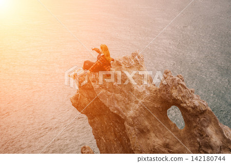 Woman hiker sunset young redhead adventurer sits on a coastal rock formation taking a photo of the sea at golden hour Woman hiker sunset young redhead adventurer sits on a coastal rock formation taking a photo of the sea at golden hour 142180744