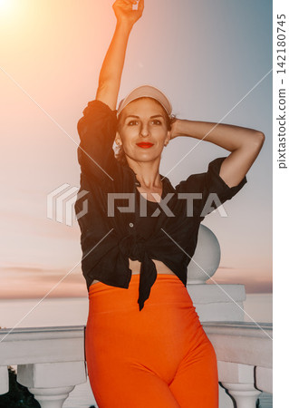 Vibrant young woman posing outdoors on a white balcony during a scenic sunset 142180745