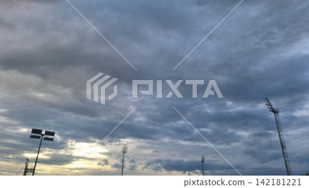 Slightly blurry shot captures warm sunset light breaking through clouds behind stadium floodlight towers Slightly blurry shot captures warm sunset light breaking through clouds behind stadium floodlight towers 142181221