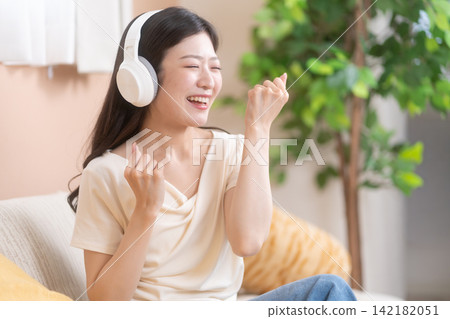 一位年輕女子戴著耳機聽音樂,臉上洋溢著笑容,看起來很開心。 一位年輕女子戴著耳機聽音樂,臉上洋溢著笑容,看起來很開心。 142182051