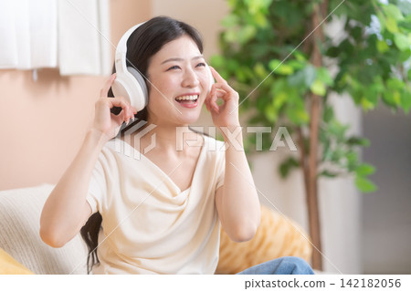 一位年輕女子戴著耳機聽音樂,臉上洋溢著笑容,看起來很開心。 一位年輕女子戴著耳機聽音樂,臉上洋溢著笑容,看起來很開心。 142182056
