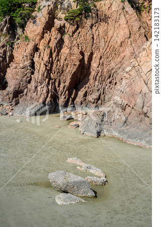 Coastal scene with a rugged cliff face rising from a shallow estuary Coastal scene with a rugged cliff face rising from a shallow estuary 142183173