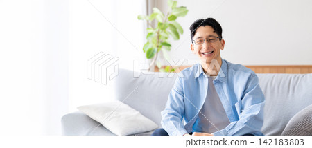 A smiling man sitting on the living room sofa. A smiling man sitting on the living room sofa. 142183803