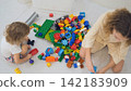 Two sisters, older and younger, sitting together playing and building with colorful construction blocks scattered on the floor. Sibling bonding concept 142183909