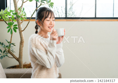 小學和中學的女孩們在家裡的客廳喝熱飲 小學和中學的女孩們在家裡的客廳喝熱飲 142184317