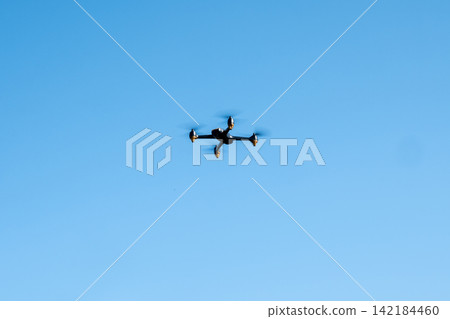 Black drone fllying in the blue sky. Innovative modern technology for work, game or entertainment. Black drone fllying in the blue sky. Innovative modern technology for work, game or entertainment. 142184460