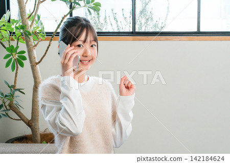 Elementary and middle school girls sitting on the sofa at home talking on their smartphones (fist pump) 142184624