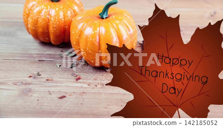 Showing two mini orange pumpkins sitting on table with maple graphic saying Happy Thanksgiving Day Showing two mini orange pumpkins sitting on table with maple graphic saying Happy Thanksgiving Day 142185052
