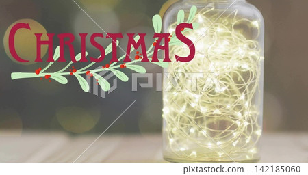Glowing glass jar holding warm lights on wood table, red CHRISTMAS with green sprig, copy space Glowing glass jar holding warm lights on wood table, red CHRISTMAS with green sprig, copy space 142185060