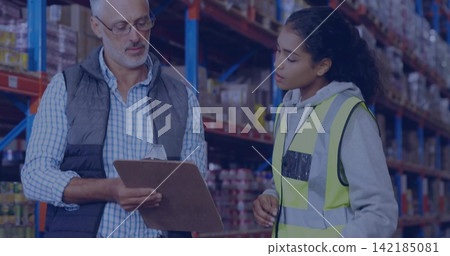 Reviewing supervisor and associate holding clipboard in aisle, wearing safety vest with racking. Warehouse, teamwork, supervision, inventory, logistics, organization, efficiency 142185081