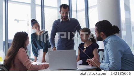 Leading leader standing behind laptop guiding team in modern meeting room, wearing business-casual Leading leader standing behind laptop guiding team in modern meeting room, wearing business-casual 142185666