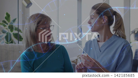 Explaining caregiver in light-blue medical scrubs holding white pill bottle on sofa, DNA overlay. Home, senior, nurse, dialogue, calm, daylight, plant Explaining caregiver in light-blue medical scrubs holding white pill bottle on sofa, DNA overlay. Home, senior, nurse, dialogue, calm, daylight, plant 142185685