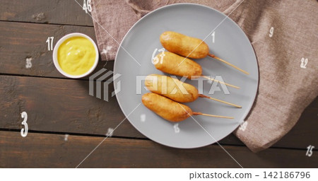 Displaying four corn dogs on skewers on gray plate with mustard ramekin on dark plank table Displaying four corn dogs on skewers on gray plate with mustard ramekin on dark plank table 142186796