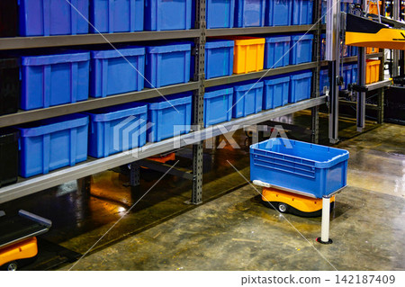 Automated guided vehicle AGV robot carrying storage bin in modern smart warehouse facility Automated guided vehicle AGV robot carrying storage bin in modern smart warehouse facility 142187409