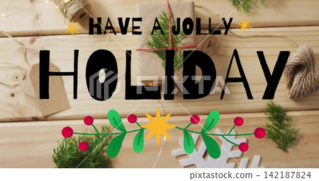 Displaying bold HOLIDAY lettering on wooden tabletop, with holly garland, kraft gift and twine Displaying bold HOLIDAY lettering on wooden tabletop, with holly garland, kraft gift and twine 142187824