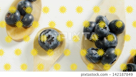 Displaying three wooden spoons holding blueberries on pale white countertop, with yellow sunbursts Displaying three wooden spoons holding blueberries on pale white countertop, with yellow sunbursts 142187849