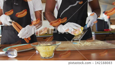 Holding hot dog sausages, staff grating cheese with grater at counter, wearing black aprons, gloves Holding hot dog sausages, staff grating cheese with grater at counter, wearing black aprons, gloves 142188083