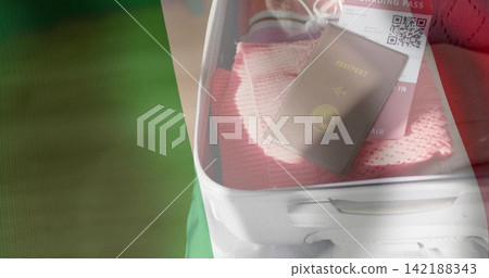 Displaying open white carry-on bag holding pink knit sweater at airport, dark passport and QR pass Displaying open white carry-on bag holding pink knit sweater at airport, dark passport and QR pass 142188343