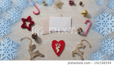 Resting red wooden heart ornament lying on light table, with sealed envelopes and snowflake cutouts Resting red wooden heart ornament lying on light table, with sealed envelopes and snowflake cutouts 142188344