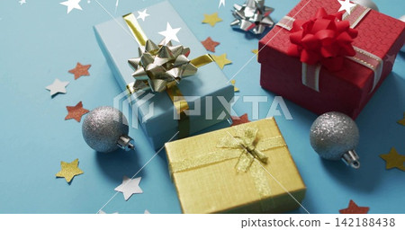 Displaying three wrapped gifts arranged on light-blue table, with silver baubles and star confetti Displaying three wrapped gifts arranged on light-blue table, with silver baubles and star confetti 142188438