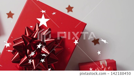 Displaying large red gift box with glossy metallic star bow on pale grey tabletop, gold confetti Displaying large red gift box with glossy metallic star bow on pale grey tabletop, gold confetti 142188450