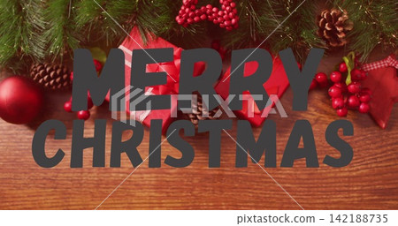 Showing large centered MERRY CHRISTMAS text overlay on wood tabletop with pine garland bauble gifts Showing large centered MERRY CHRISTMAS text overlay on wood tabletop with pine garland bauble gifts 142188735