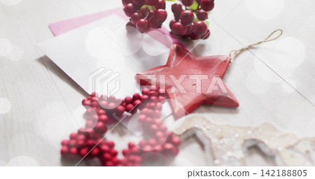 Displaying red star ornament resting on light wood tabletop, showing beaded star, berries, envelope Displaying red star ornament resting on light wood tabletop, showing beaded star, berries, envelope 142188805