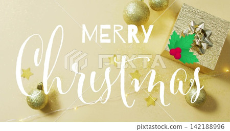 Showing white handwritten Merry Christmas script on gold backdrop with gift box, silver bow, holly Showing white handwritten Merry Christmas script on gold backdrop with gift box, silver bow, holly 142188996