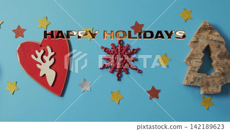 Placing red heart snowflake carved tree on blue backdrop adding star confetti metal HAPPY HOLIDAYS 142189623