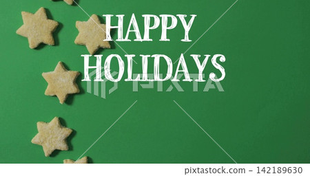 Displaying large decorative white HAPPY HOLIDAYS text centered on green backdrop, with star cookies Displaying large decorative white HAPPY HOLIDAYS text centered on green backdrop, with star cookies 142189630